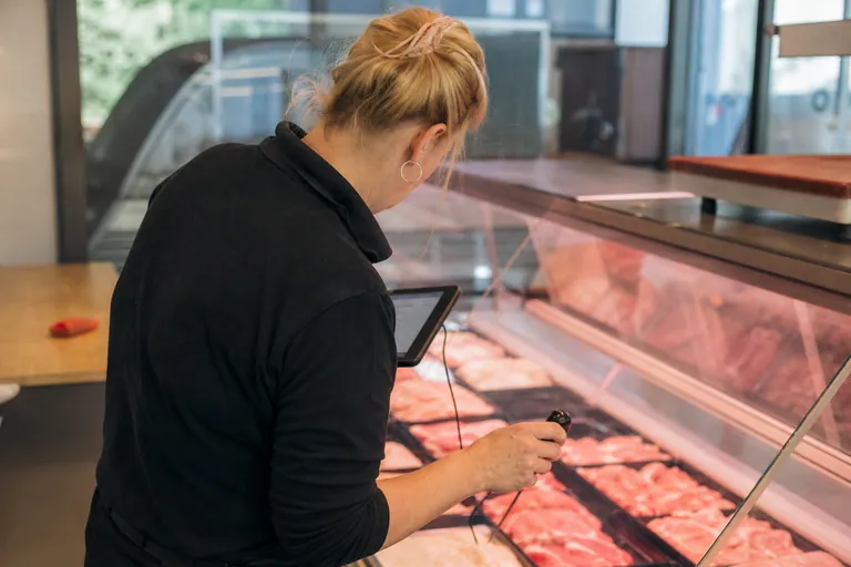 Mitarbeiterin misst die Temperatur an einer Kühltheke und trägt den Wert auf einem Tablet ein