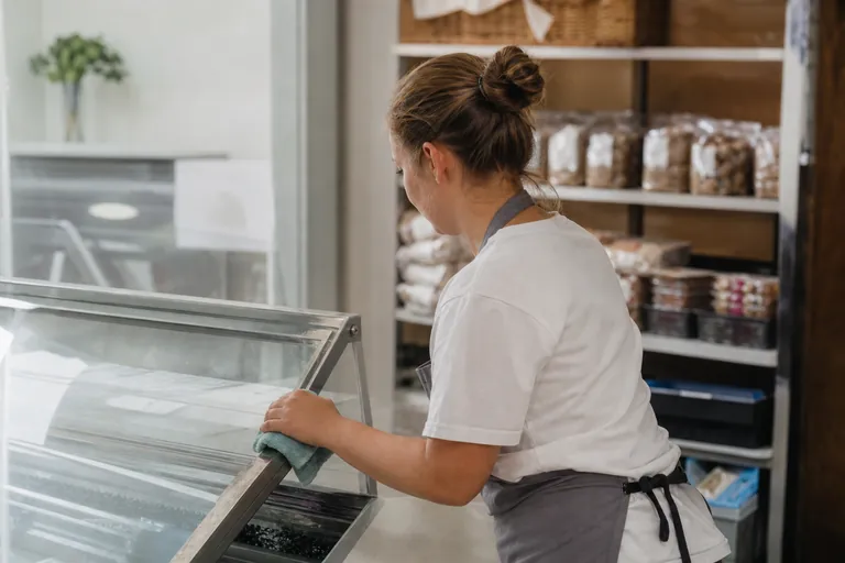 Mitarbeiterin reinigt eine Kühltheke in einer Bäckerei