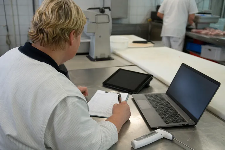 Papierliste, Laptop mit Tabelle und Tablet liegen neben einem Kühlthermometer auf einem Arbeitstisch