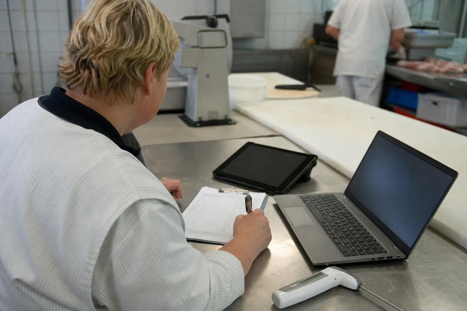Papierliste, Laptop mit Tabelle und Tablet liegen neben einem Kühlthermometer auf einem Arbeitstisch